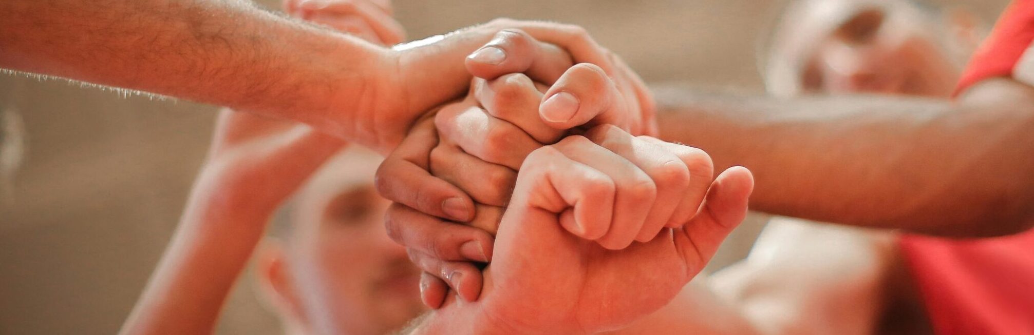 From below of crop multiethnic team of professional basketball players gathering and putting hands together while standing on playground before game